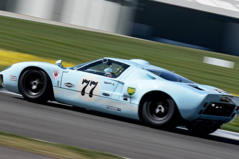 A light blue Ford GT40 races down the track, its number 77 prominently displayed.