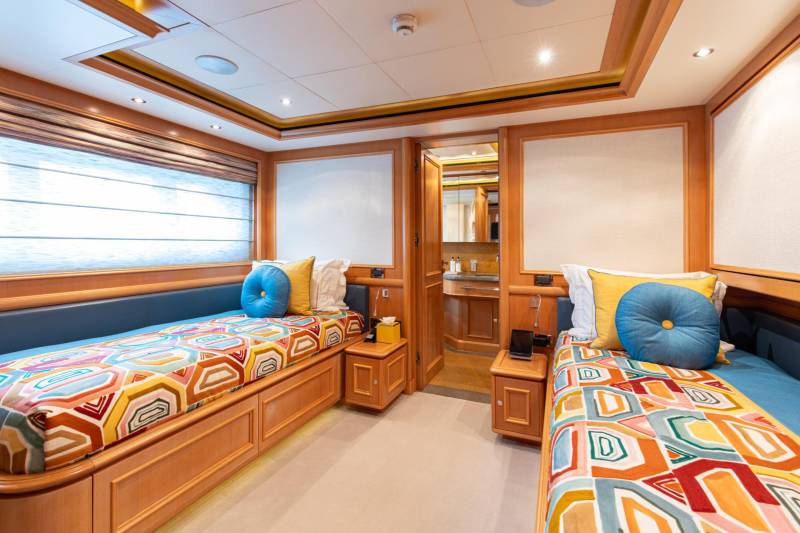 Colorful geometric bedding adorns twin beds in a luxurious yacht cabin with a view of the water.