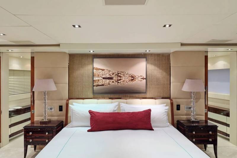 Luxurious yacht cabin features a plush king-size bed adorned with crisp white linens and a striking crimson accent pillow.