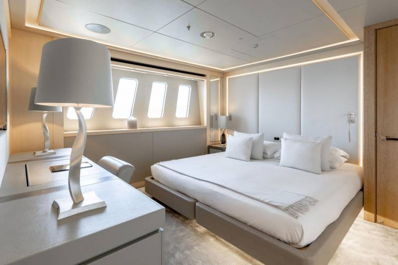 Luxurious yacht cabin features a plush bed, elegant desk, and unique porthole-style windows illuminated by ambient lighting.