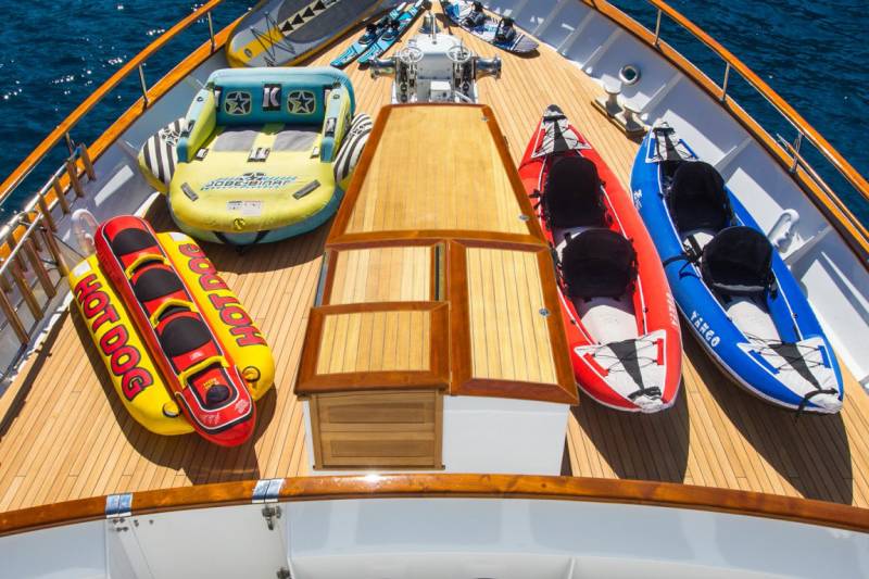 A collection of inflatable water toys and kayaks are neatly arranged on the wooden deck of a luxurious yacht.