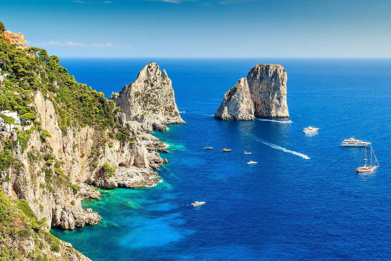 Boats dot the azure waters surrounding the dramatic cliffs and iconic sea stacks of Capri.