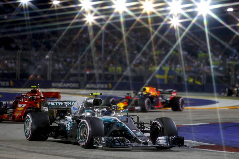 The image shows a Formula One race taking place at night, with the cars speeding through the track under the bright spotlights illuminating the scene.