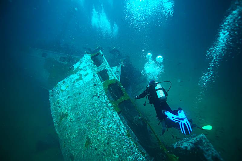 A diver explores the eerie depths of a sunken shipwreck, surrounded by a cloud of rising bubbles.