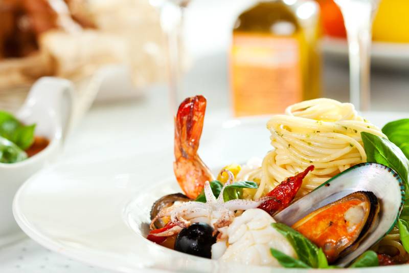 Savor a delectable seafood pasta dish, a vibrant medley of shrimp, mussels, calamari, and sun-dried tomatoes, artfully arranged with fresh basil.