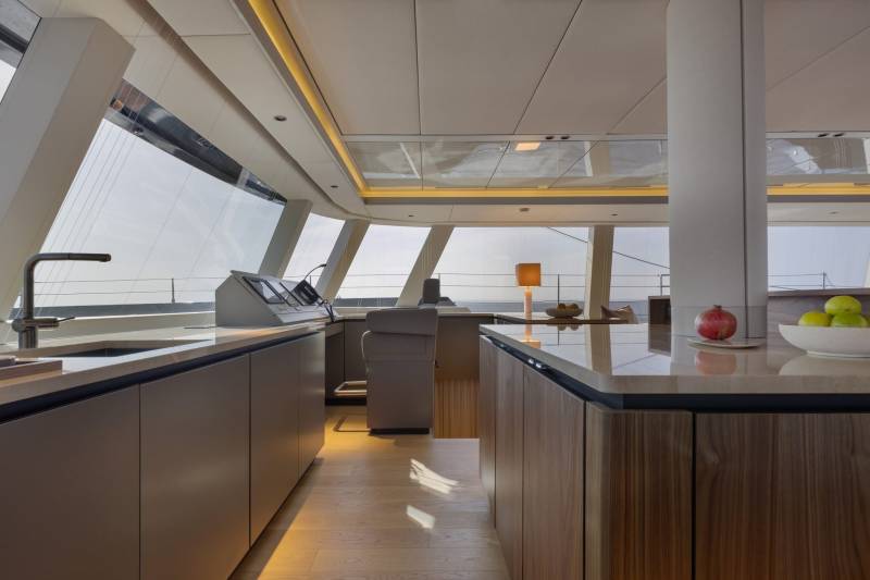 Sunlight streams across the polished wood floor of this modern yacht galley, highlighting the sleek cabinetry and expansive windows.