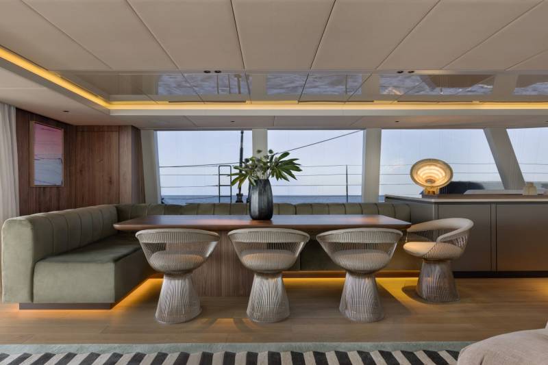A sleek dining area on a yacht features a plush banquette, modern chairs, and a large window overlooking the ocean.
