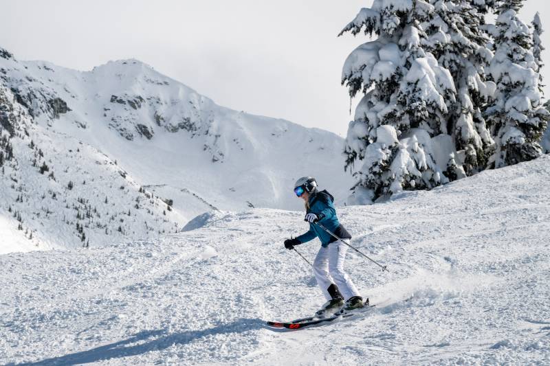 A skier carves down a snow-covered mountain slope, leaving a trail of powder in their wake.