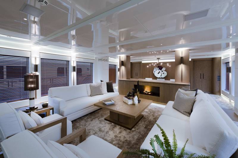 Luxurious yacht salon features plush white sofas, a modern fireplace, and warm wood accents.