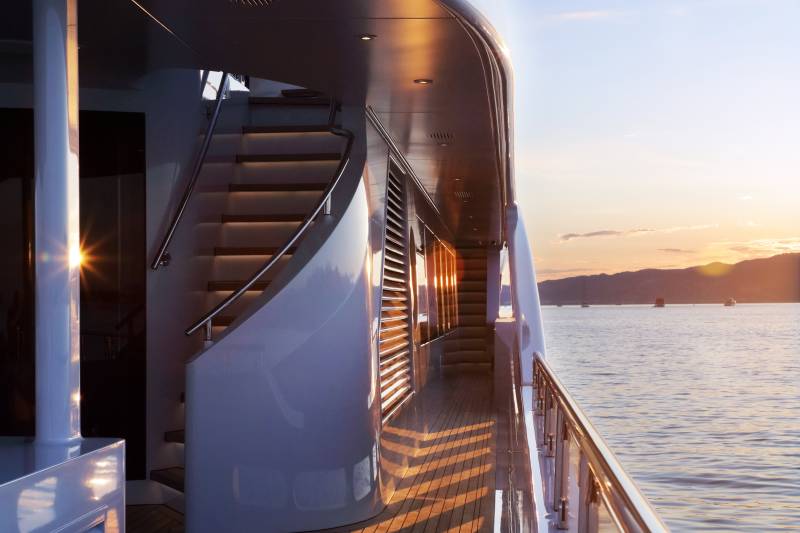 Golden hour light casts dramatic shadows across the deck of a luxurious yacht as it sails on calm waters.