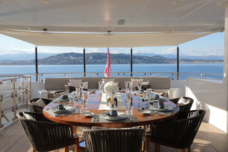 An elegant outdoor dining setting on a yacht overlooks a picturesque coastal town.