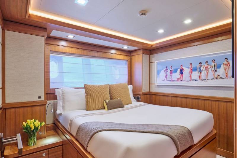A luxurious yacht cabin features a comfortable bed, warm wood accents, and a vintage beach photograph.