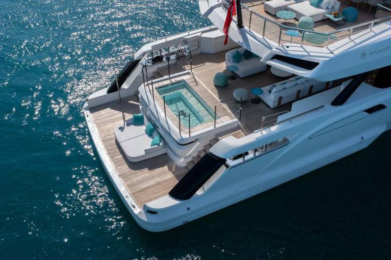 A luxurious yacht with a sparkling pool and plush seating areas floats on the shimmering blue ocean.