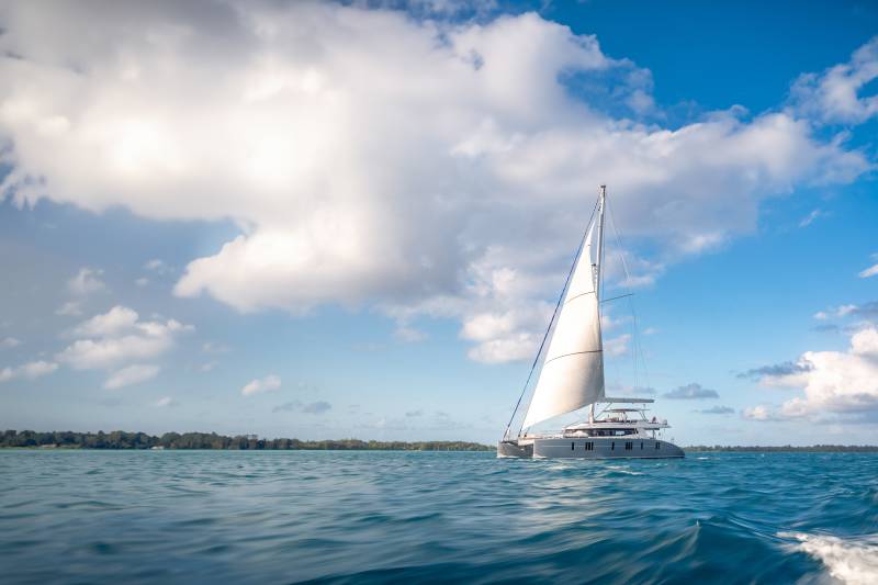A sleek catamaran glides across the turquoise waters under a sky filled with dramatic clouds.
