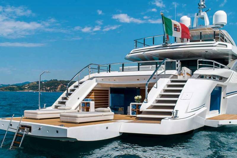 A luxurious white yacht with Italian flags proudly displayed anchors in the clear blue sea off a picturesque coastline.