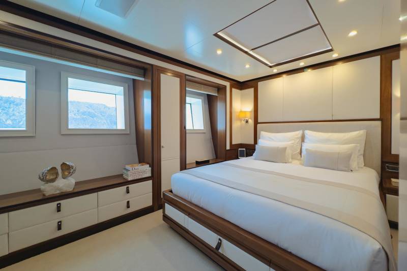 Luxurious yacht cabin features a spacious bed, elegant wood accents, and stunning ocean views from the windows.