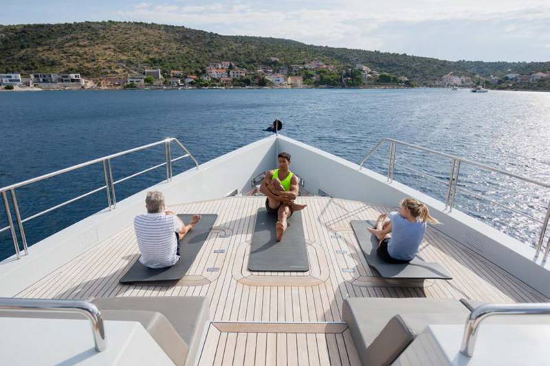 Three people practice yoga on the deck of a yacht overlooking a coastal village.