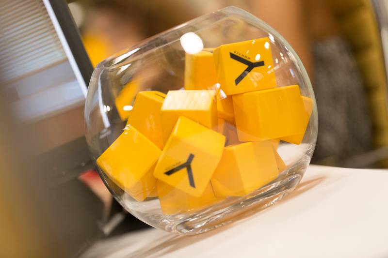 A glass container filled with bright yellow cubes, likely some type of cheese or food item, sits on a blurred background.