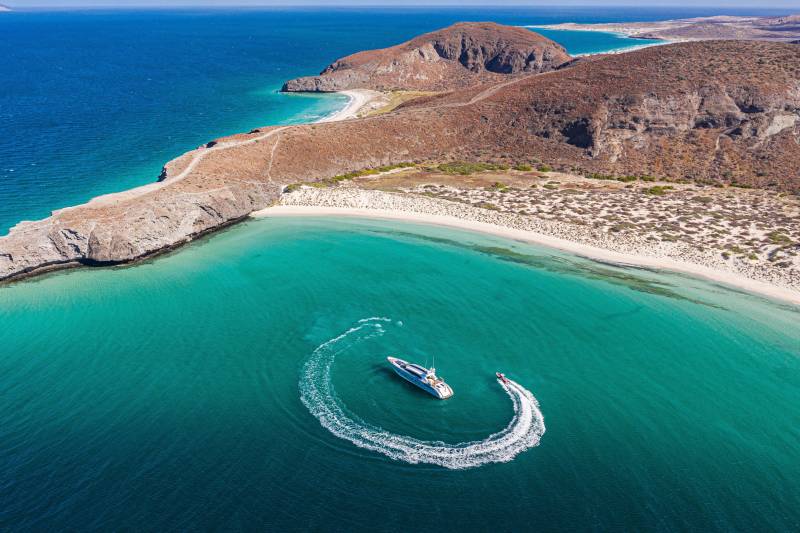 A luxurious yacht and jet ski carve through the crystal-clear turquoise waters of a secluded bay.