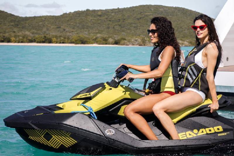 Two women enjoy a thrilling jet ski ride on a turquoise ocean with a lush green island in the background.