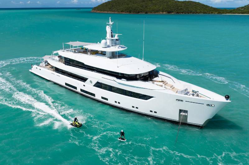 A luxurious white yacht floats in turquoise waters as two people enjoy jet skis and a hydrofoil nearby.