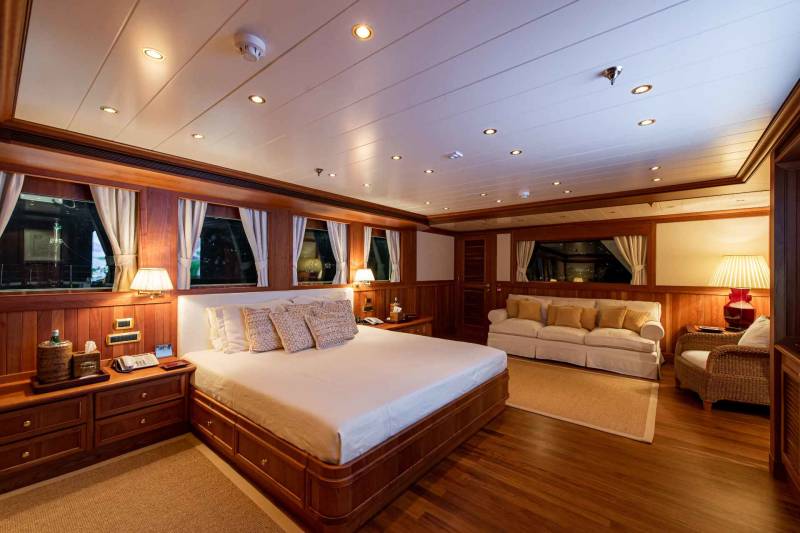 Luxurious wood-paneled stateroom aboard a yacht features a king-sized bed, plush seating, and ample natural light.