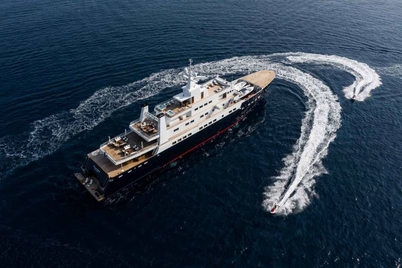 A luxurious yacht cruises through the deep blue sea, trailed by two energetic jet skiers.