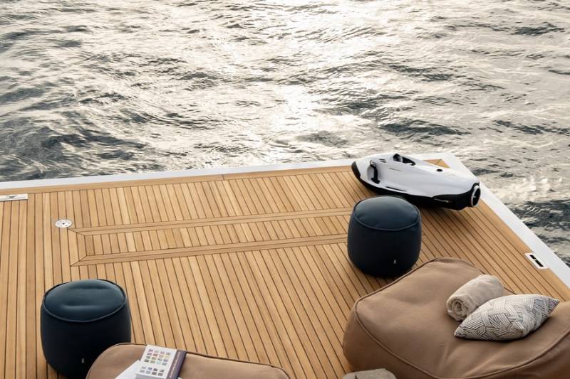 A sleek white watercraft rests on a teak deck beside comfortable seating overlooking the shimmering ocean.