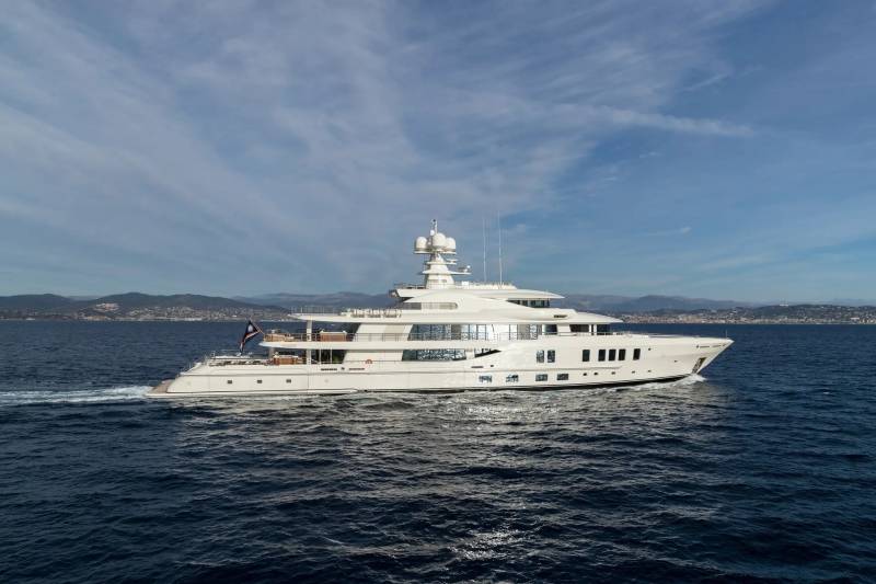 A luxurious white yacht glides through the deep blue sea under a cloudy sky with distant hills.