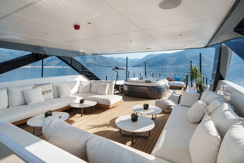 Luxurious white sofas and a hot tub offer the perfect spot to relax on this yacht's deck with a stunning mountain and sea view.
