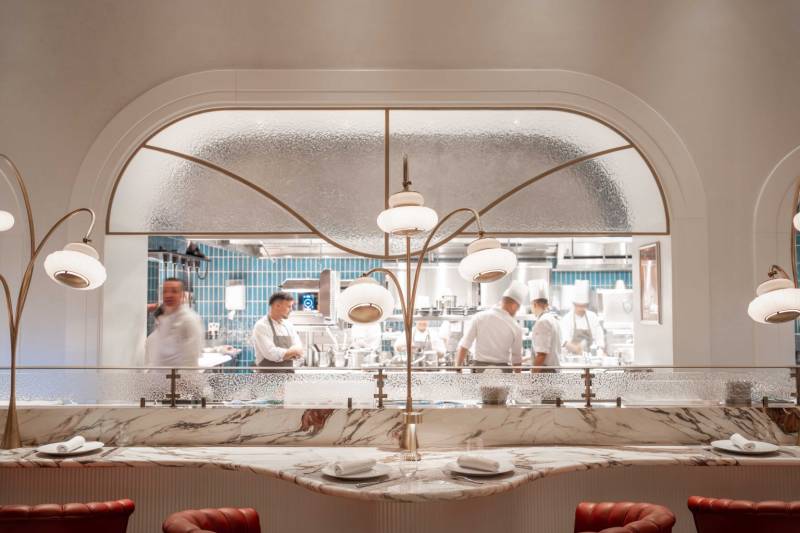 Chefs work diligently in a gleaming open kitchen visible through a frosted glass partition at this elegant restaurant.