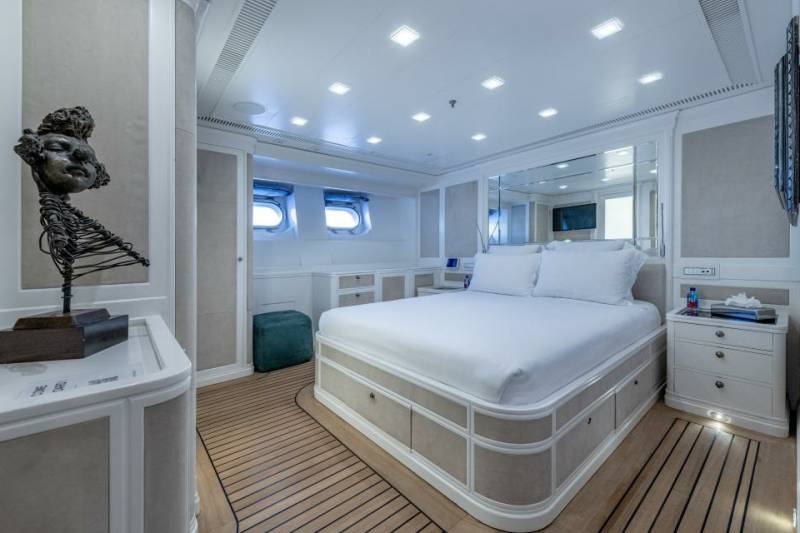 Luxurious yacht stateroom features a plush bed, elegant decor, and porthole windows offering ocean views.