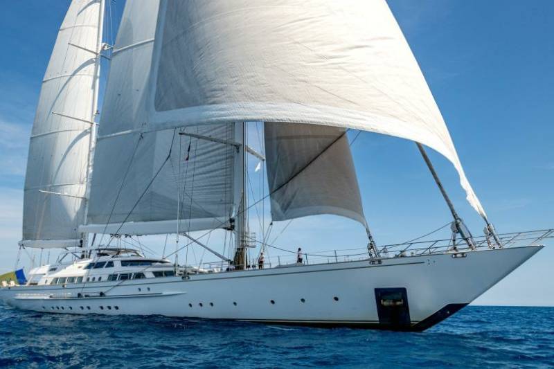 A majestic white sailing yacht glides across the deep blue ocean under a clear sky.