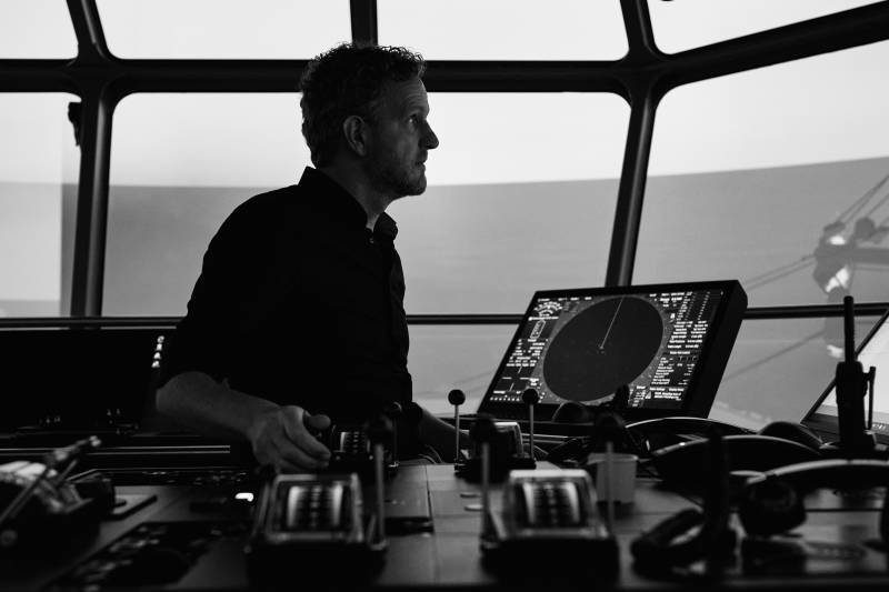A ship's captain navigates the open sea from the bridge, surrounded by advanced radar and navigation systems.