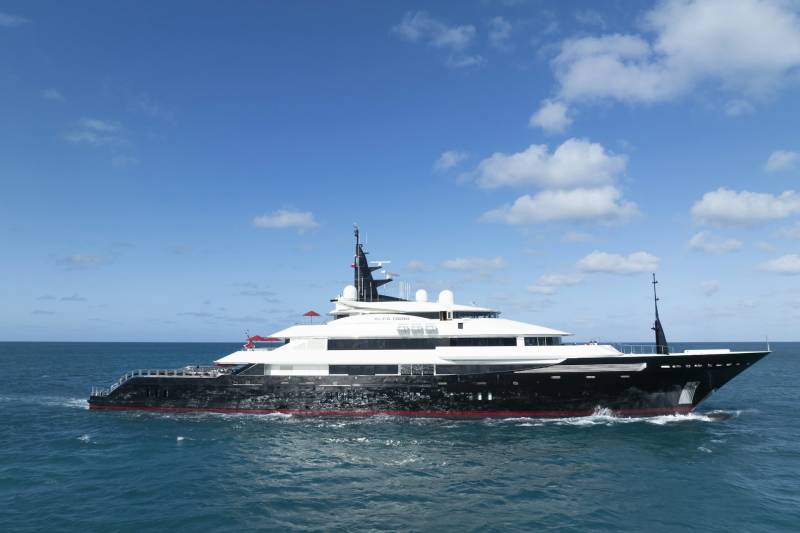 The sleek Alfa Nero superyacht glides through the vibrant blue ocean under a sky dotted with fluffy white clouds.