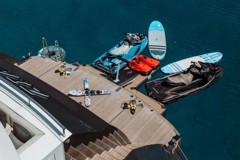 A luxury yacht is equipped with a variety of watercraft, including jet skis and paddleboards, ready for adventure on the open sea.