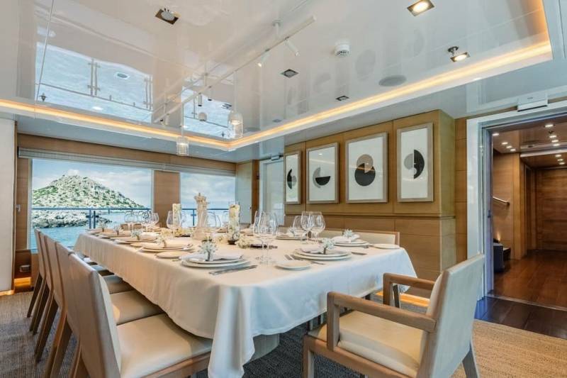 A formal dining table is set for a special occasion aboard a luxurious yacht, overlooking a scenic coastal view.