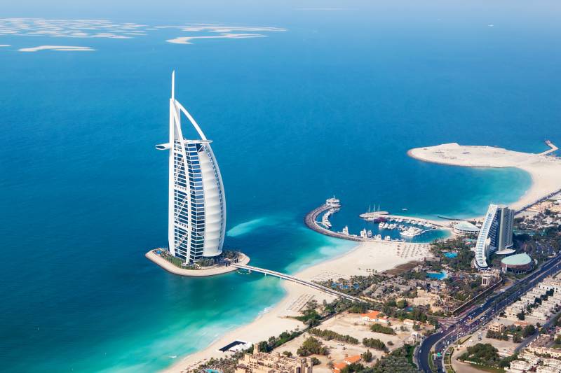 An aerial view captures the iconic sail-shaped Burj Al Arab hotel and the man-made islands of Dubai against a backdrop of the turquoise Arabian Gulf.