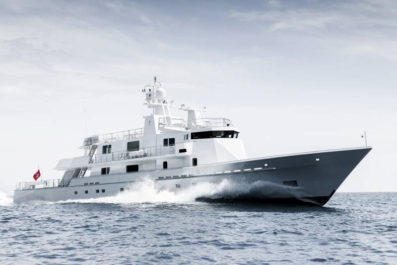 A sleek white yacht cuts through the choppy blue sea, leaving a powerful wake under a pale, cloudy sky.