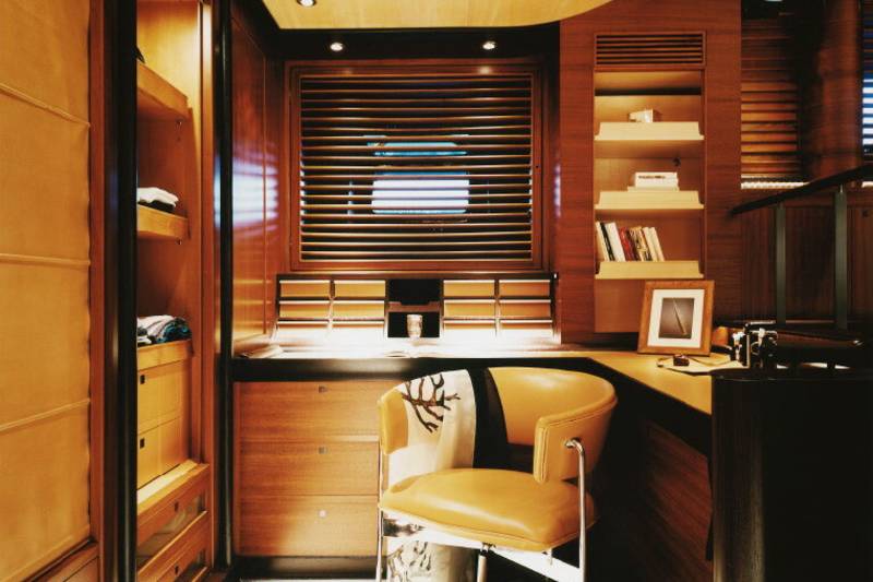 A stylish office space features warm wood tones, a comfortable leather chair, and a window with horizontal blinds.