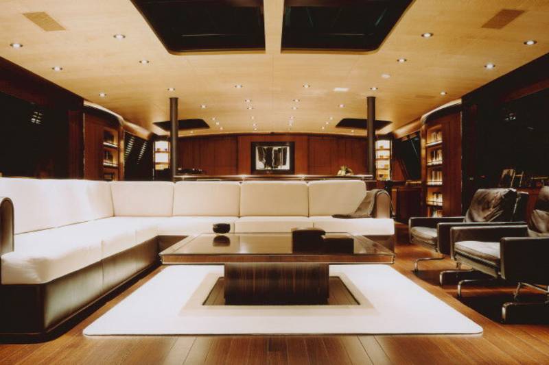 Luxurious yacht interior features a plush white sectional sofa, a modern coffee table, and dark leather armchairs.