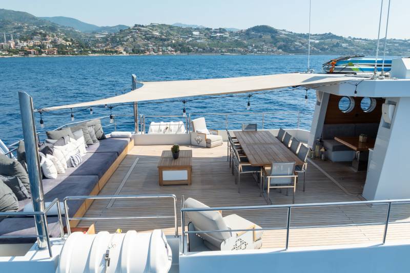 Relax on the spacious deck of this yacht, complete with comfortable seating and an outdoor dining area, overlooking a picturesque coastal town.