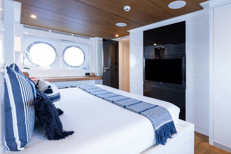 Luxurious yacht cabin features a comfortable bed, large porthole windows, and a sleek entertainment center.