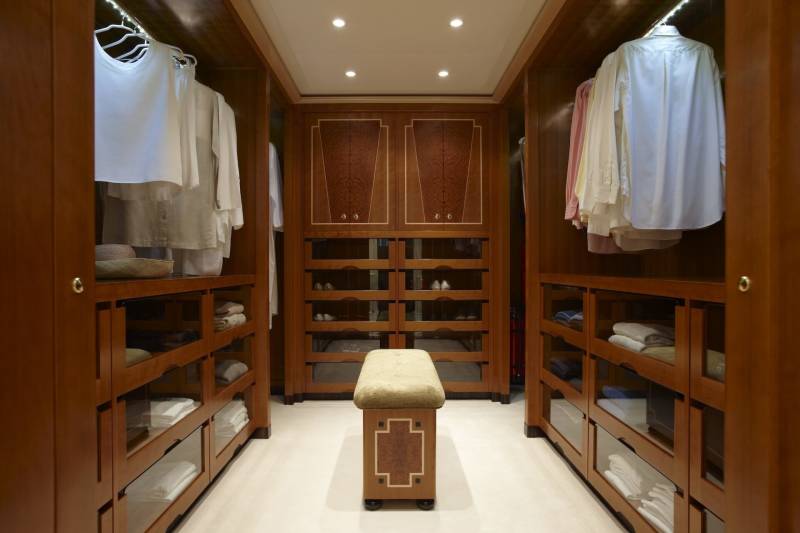 This luxurious walk-in closet features polished wood cabinetry, organized shelves, and a plush bench for a refined dressing experience.