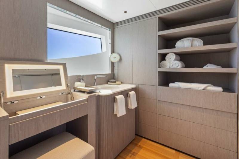 A modern bathroom with a vanity, sink, and ample storage is illuminated by natural light from a large window.