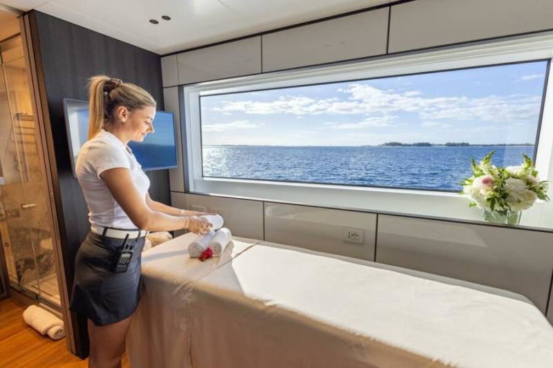 A spa attendant prepares a massage table with fresh towels overlooking a serene ocean view.