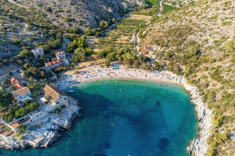 Sunbathers relax on a pebble beach beside the crystal-clear turquoise waters of a secluded bay.