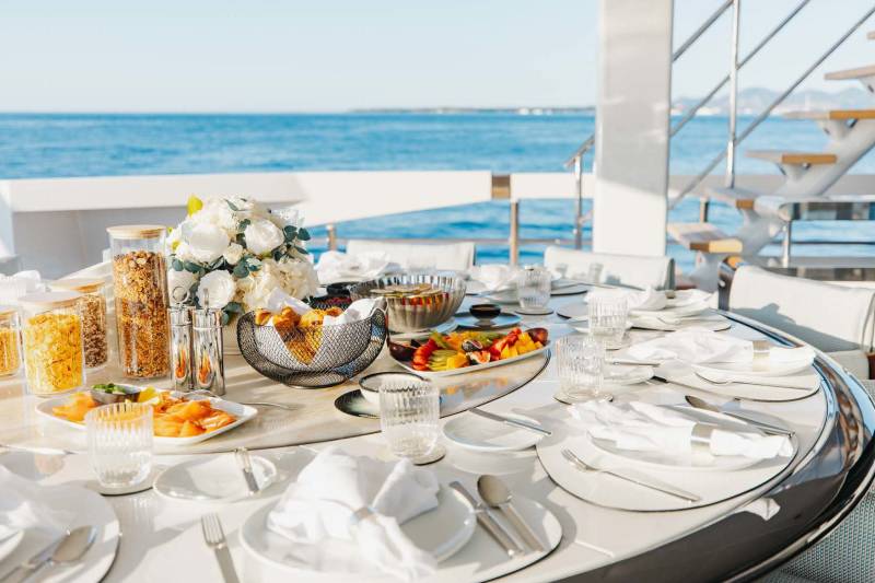 A beautifully set table on a yacht offers a delightful breakfast spread with a stunning ocean view.
