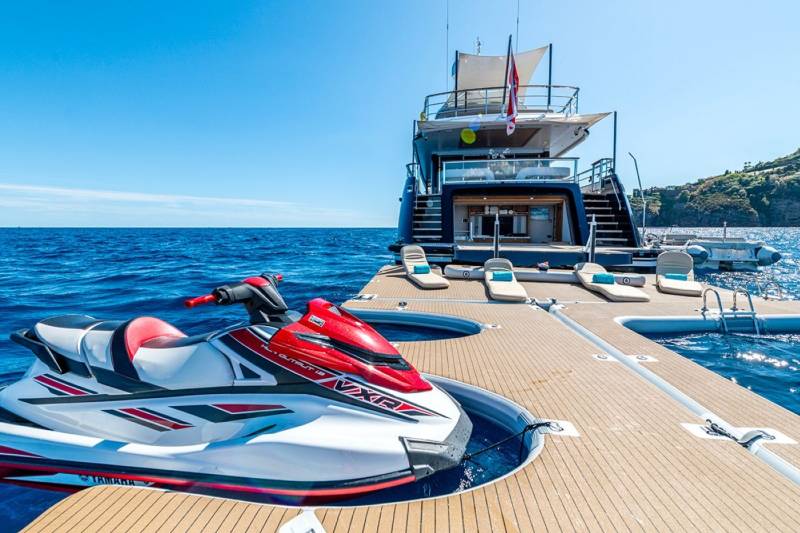 A sleek jet ski rests on a floating dock beside a luxurious yacht under a clear blue sky.