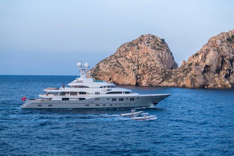 A luxury yacht cruises through the azure waters near a rugged, rocky island.
